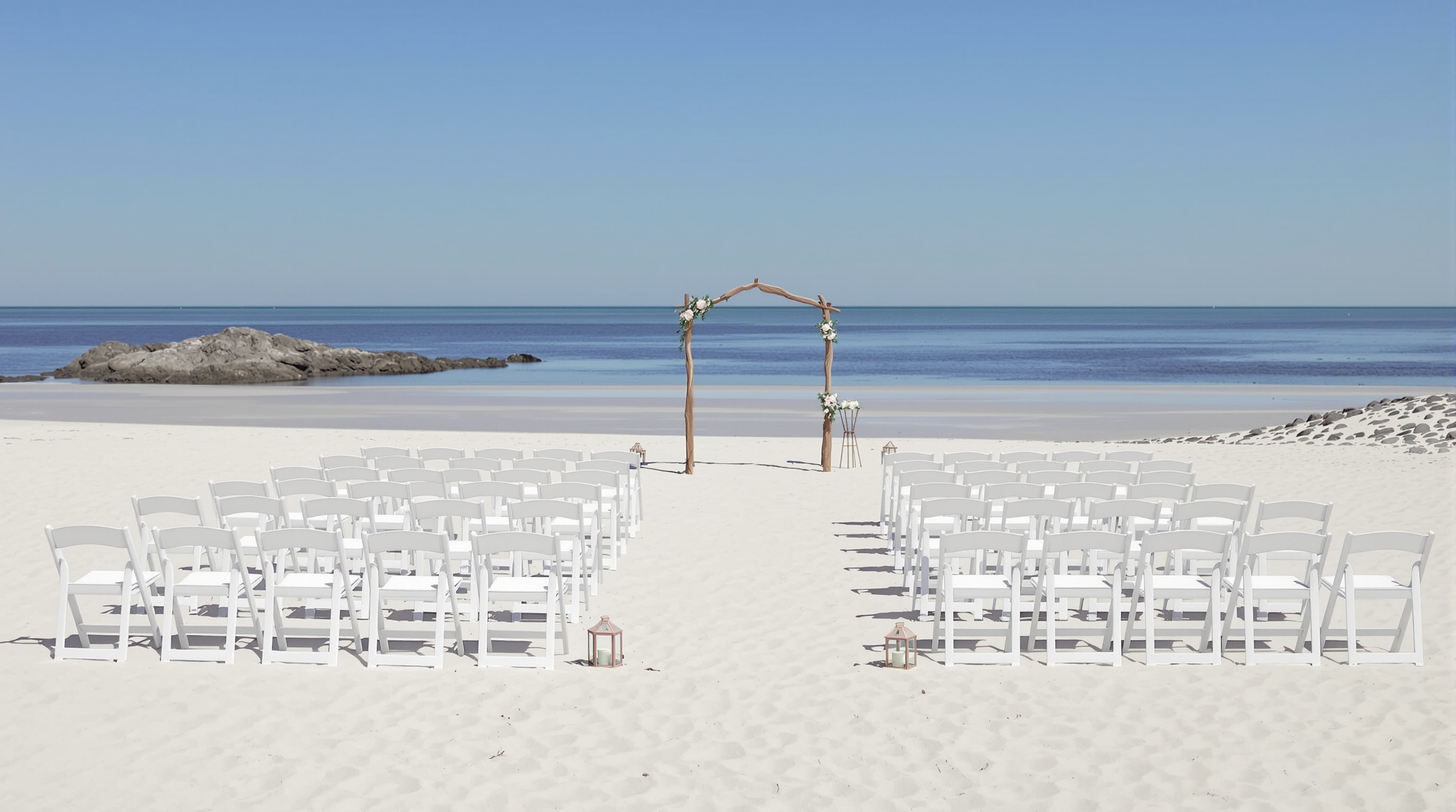White folding chairs and a small setup arranged neatly on wide firm sand at low tide under a clear sky